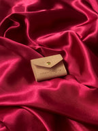 Travel sized light pink pouch with a brand logo on a red satin background