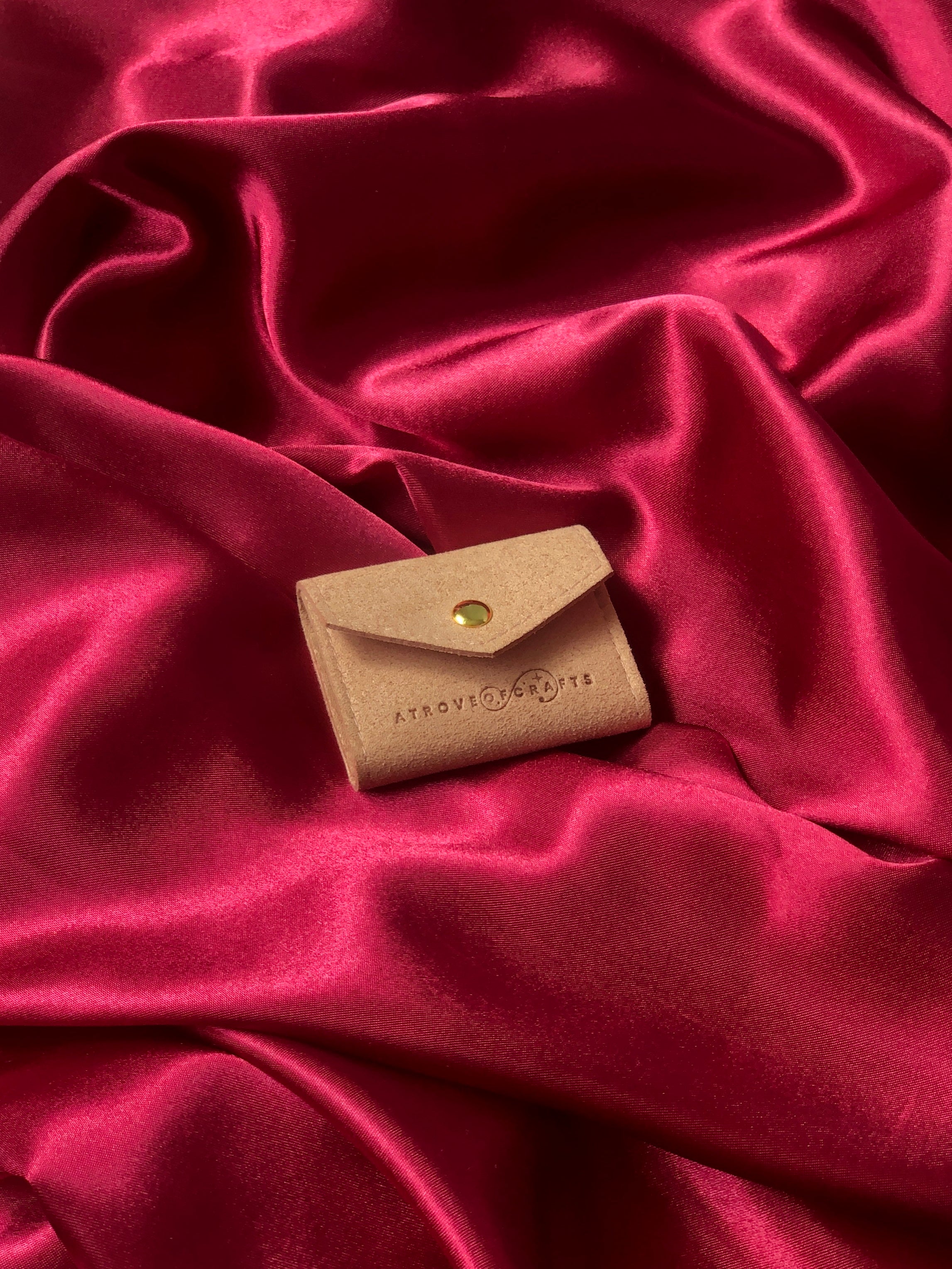 Travel sized light pink pouch with a brand logo on a red satin background