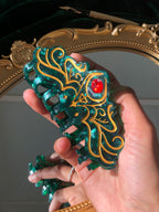 Decorative comb with intricate design and red gem held by a hand in front of a mirror.
